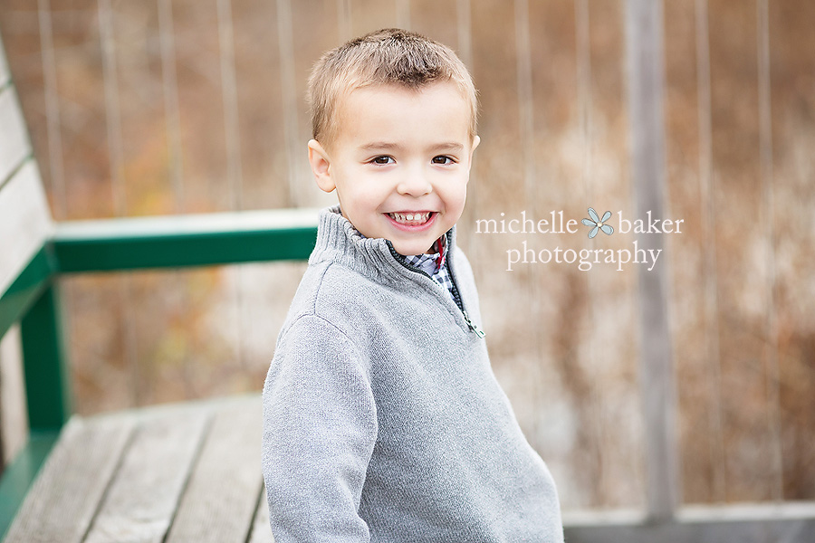 Little boy in grey sweater smiling sitting on a bench