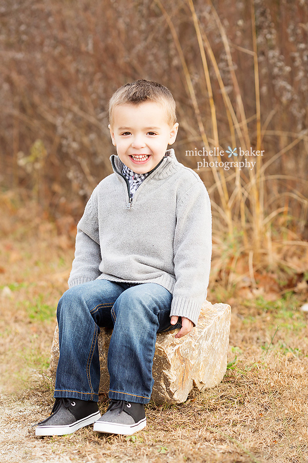 Little boy in grey sweater smiling sitting on a rock